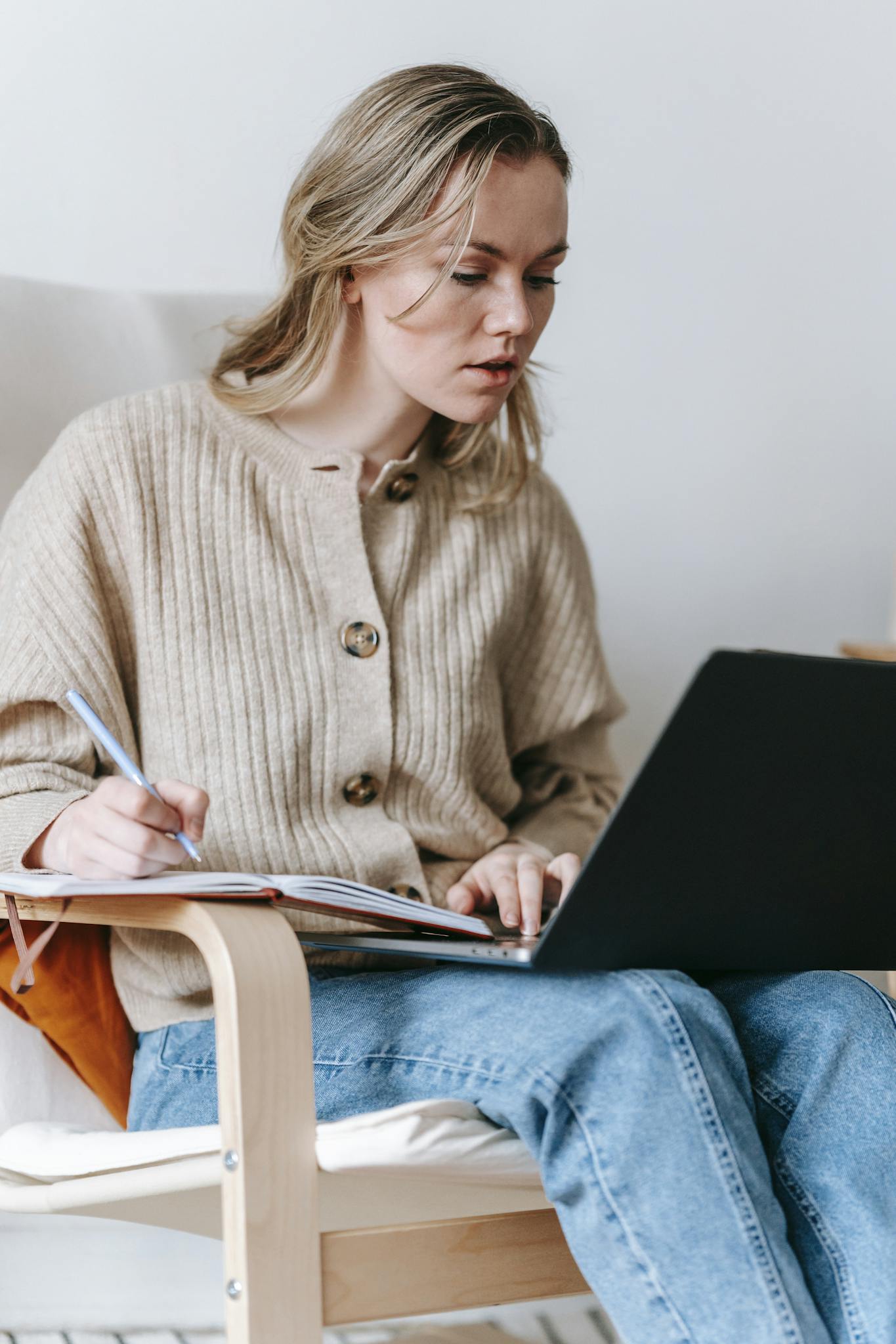 Woman attentively working on laptop and taking notes at home office.